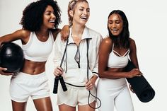 three beautiful women standing next to each other holding yoga mats and exercise equipment in their hands