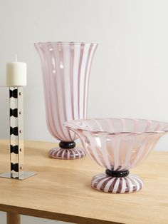 two pink glass vases sitting on top of a wooden table next to a candle