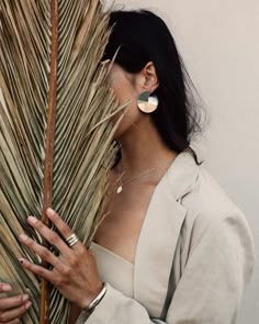 a woman holding a palm tree with her hands on the top of it and wearing earrings