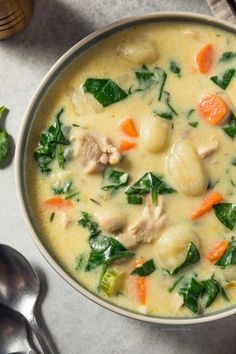 a bowl of soup with meat, spinach and carrots next to a spoon