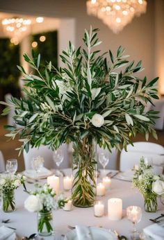 a vase filled with lots of greenery sitting on top of a table