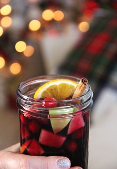 a person holding a glass jar filled with fruit and cinnamon stick in front of a christmas tree