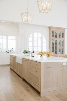 a large kitchen with wooden cabinets and white counter tops, along with two chandeliers hanging from the ceiling