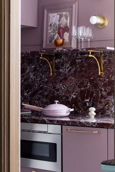 a kitchen with purple walls and marble counter tops, gold faucets and wine glasses