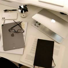 an apple computer sitting on top of a white desk next to a notebook and eyeglasses