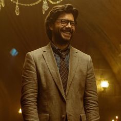 a man in a suit and tie smiles at the camera while standing in front of a chandelier