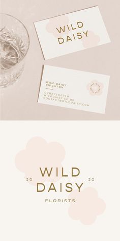 two business cards with the words wild daisy in gold foil on them next to a glass of water