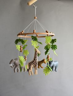 an animal mobile is hanging from the ceiling in front of a gray wall with green leaves and two giraffes