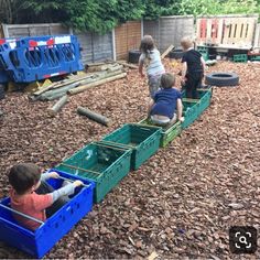 three children are playing in a toy train on the ground with wood chips all around