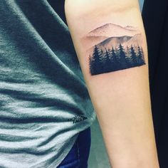 a person with a tattoo on their arm that has trees and mountains in the background