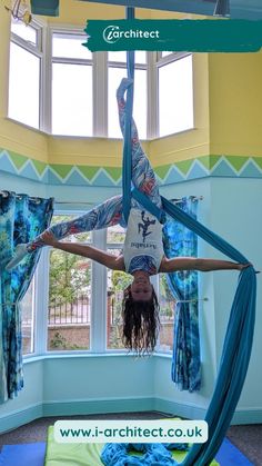 a woman is doing aerial acrobatic tricks in a room with blue curtains