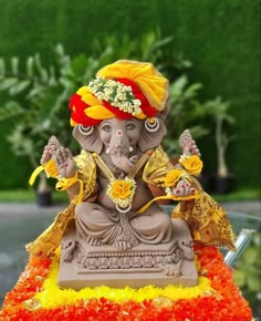 a statue of an elephant with flowers on its head sitting in the middle of a flower bed