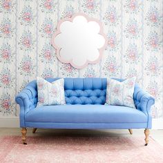 a blue couch with pink pillows in front of a floral wallpapered wall and mirror