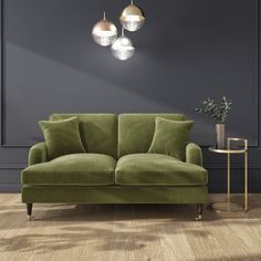 a green couch sitting on top of a hard wood floor next to a table with a potted plant