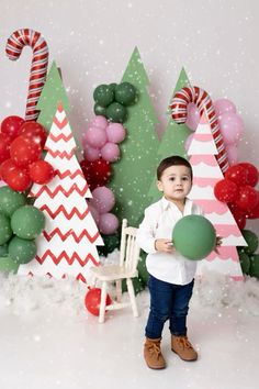 a little boy holding a balloon in front of some christmas trees and balloons on the wall