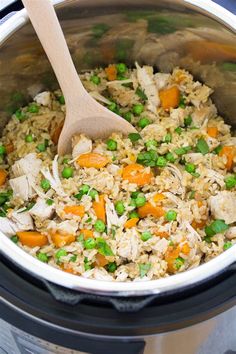 a crock pot filled with rice, peas and carrots next to a wooden spoon