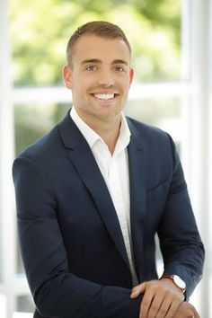 a man in a suit and white shirt is smiling at the camera with his arms crossed