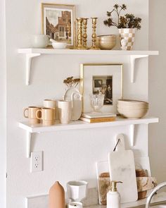 two white shelves with pictures, cups and other items on them in a living room