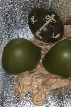 three army green helmets sitting on top of a piece of brown paper next to each other