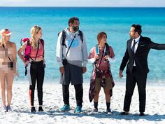 a group of people standing on top of a beach next to the ocean with one man pointing at something