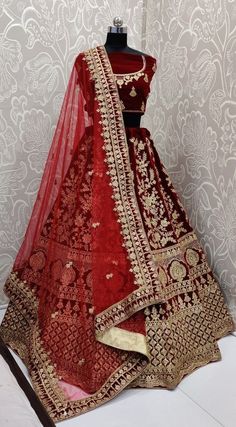 a red and gold wedding lehenga on display in front of a white wall