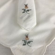 two white ties with embroidered flowers on them sitting on a tableclothed cloths