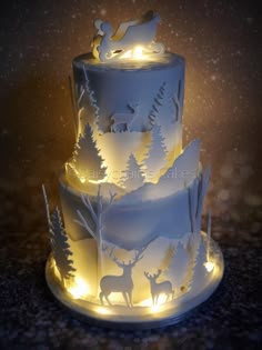 a three tiered cake decorated with white frosting and lit up reindeers on top