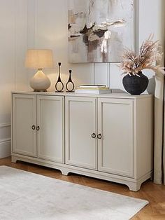 a living room with a white rug and two vases on top of the sideboard