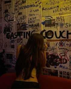 a woman sitting in front of a wall covered with graffiti and writing on it's walls