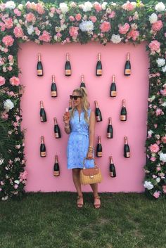 a woman standing in front of a pink wall with lots of bottles