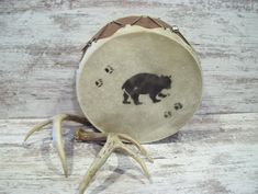 a black bear and paw prints on an old drum case with antlers around it