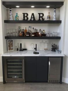 a bar with liquor bottles and glasses on the top shelf, next to an open wine cooler