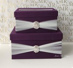 two purple boxes with white ribbons and bows on the top one has a diamond brooch