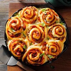 a skillet filled with cinnamon rolls on top of a wooden table next to a knife