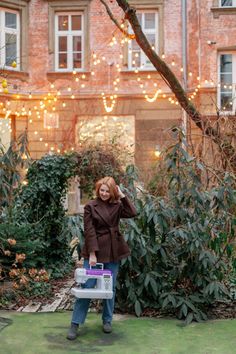 a woman standing in front of a building holding a purple and white box with lights on it