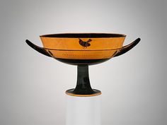 an orange and black vase with a rooster on it's side sitting on a white pedestal