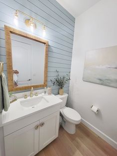 a white bathroom with blue walls and wood flooring on the wall, along with a wooden framed mirror