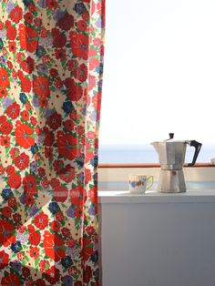 a coffee pot sitting on top of a window sill next to a flowered curtain