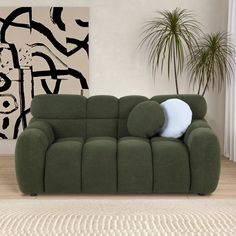 a green couch sitting on top of a wooden floor next to a potted plant