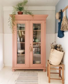 a pink china cabinet with glass doors and plants on the top shelf next to it