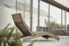 a wooden and metal chaise lounge chair sitting on a wood floor in front of a building