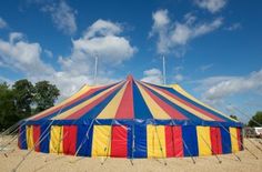 a large circus tent sitting on top of a sandy beach under a blue cloudy sky