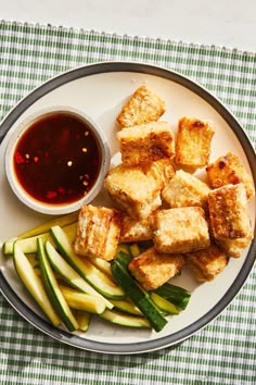 a white plate topped with tofu and cucumbers next to a dipping sauce