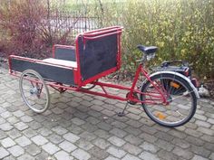 a bike with a trailer attached to it on a cobblestone walkway next to bushes