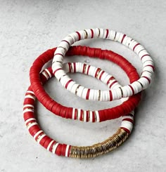 three red, white and gold bracelets on a gray surface with one bead in the middle