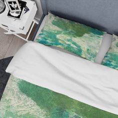 a bed with green and white sheets on top of it next to a night stand