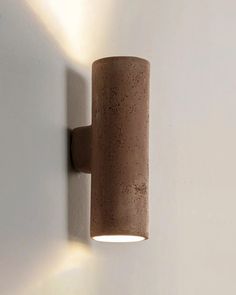 a light that is on the wall next to a white wall with a brown cylinder