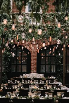 an outdoor dining area with tables and chairs covered in greenery, surrounded by hanging lights