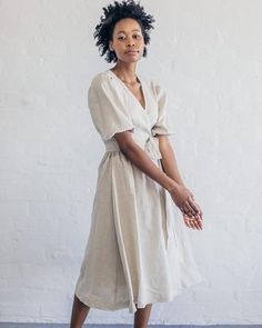 a woman standing in front of a white wall wearing a tan dress and black shoes