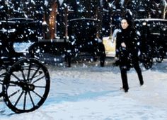 a man walking in the snow next to a horse drawn carriage